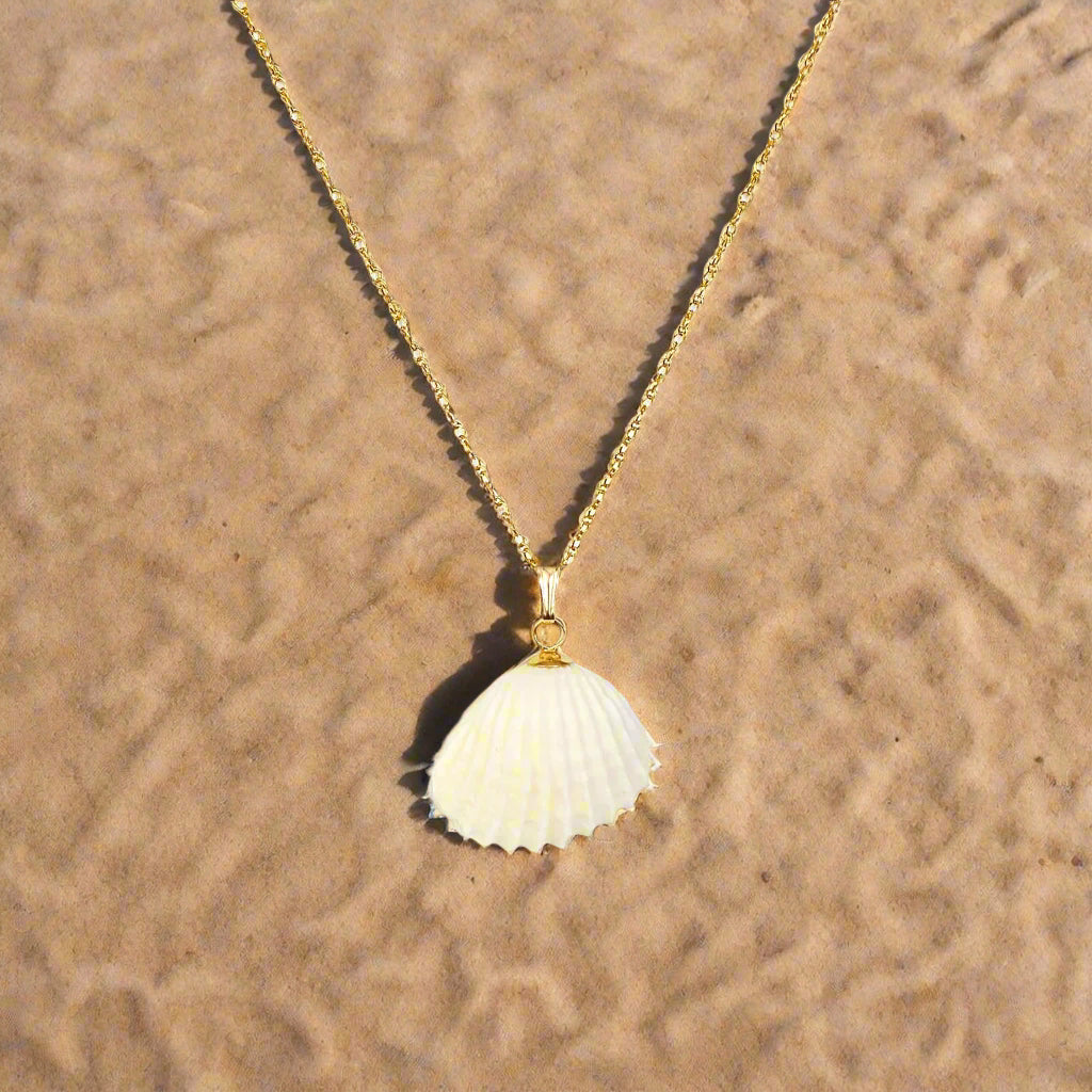 Gold necklace with a shell pendant on a sand background