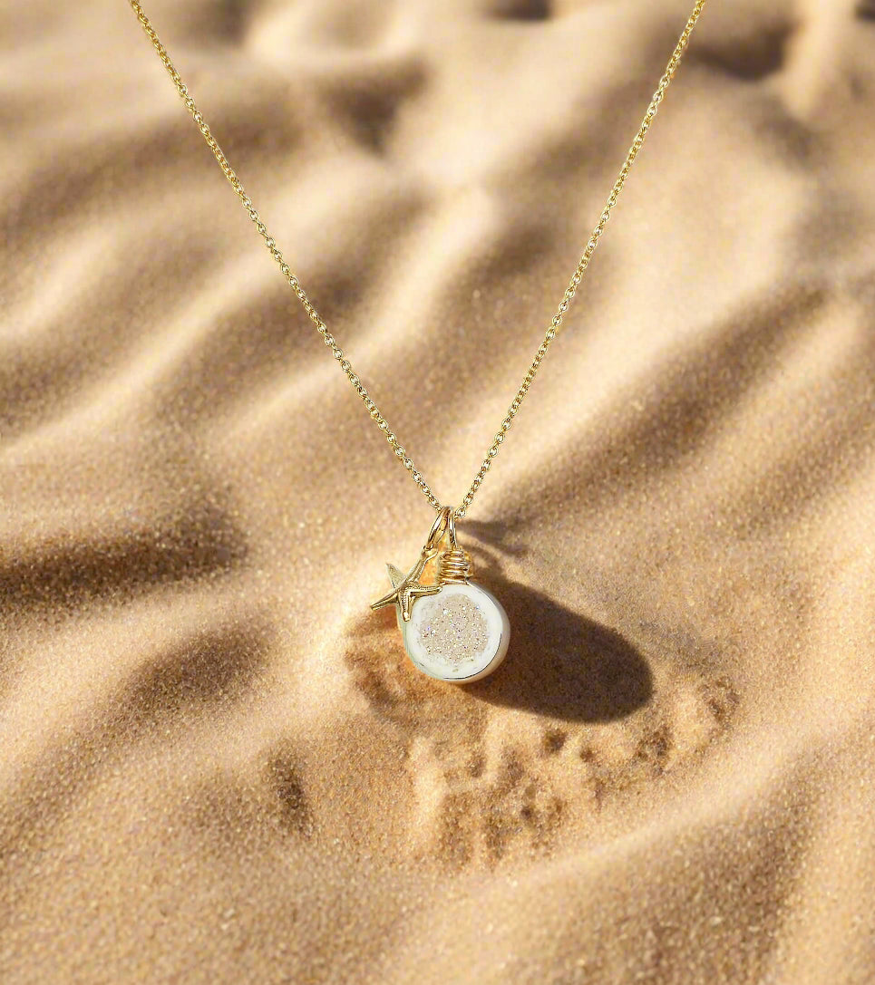 Gold necklace with a round pendant and starfish charm on a white background