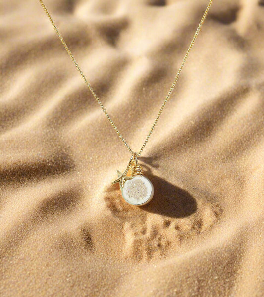 Gold necklace with a round pendant and starfish charm on a white background