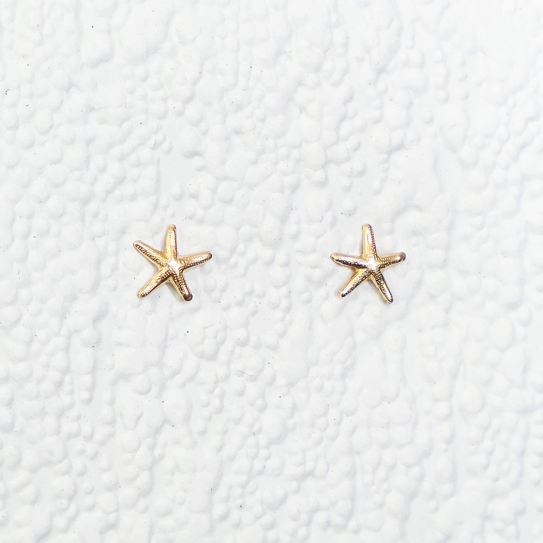 Gold star-shaped earrings on a textured white background