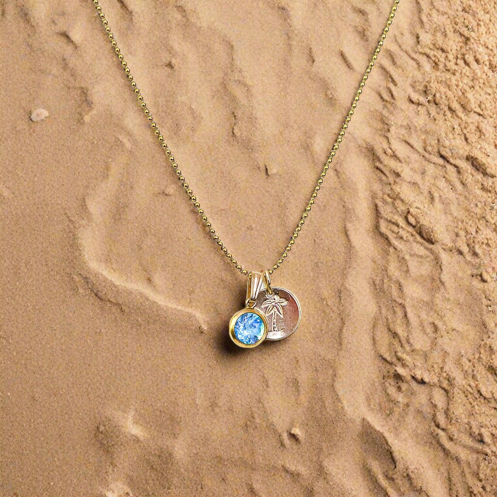 Gold necklace with a pendant featuring a blue gemstone on a sandbackground