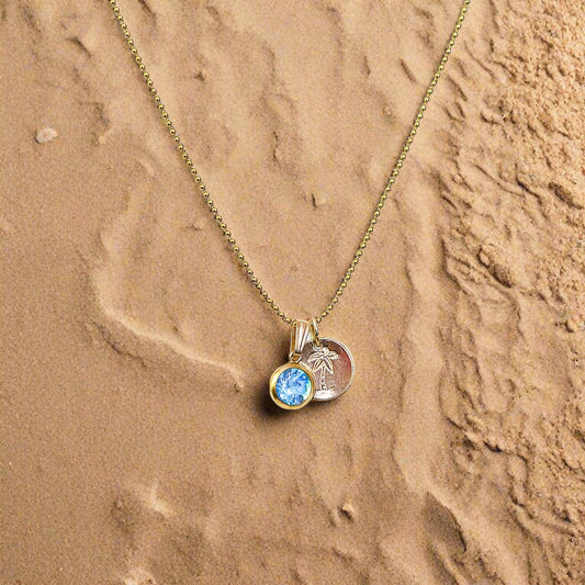 Gold necklace with a pendant featuring a blue gemstone on a sandbackground