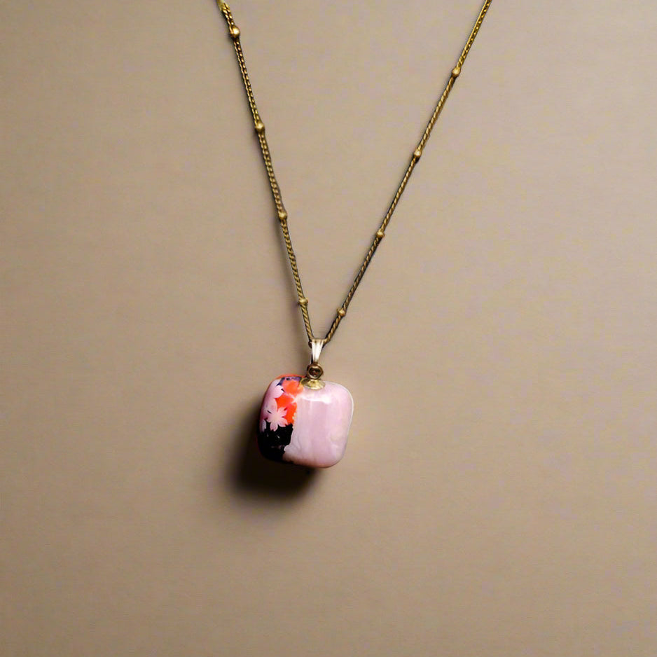 Necklace with a pink pendant featuring floral design on a beige background