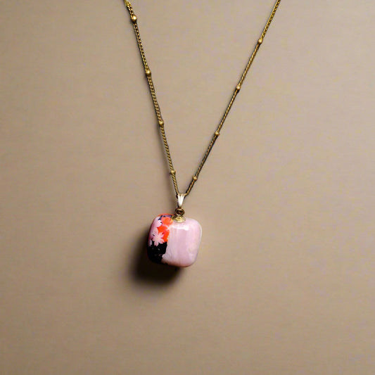 Necklace with a pink pendant featuring floral design on a beige background