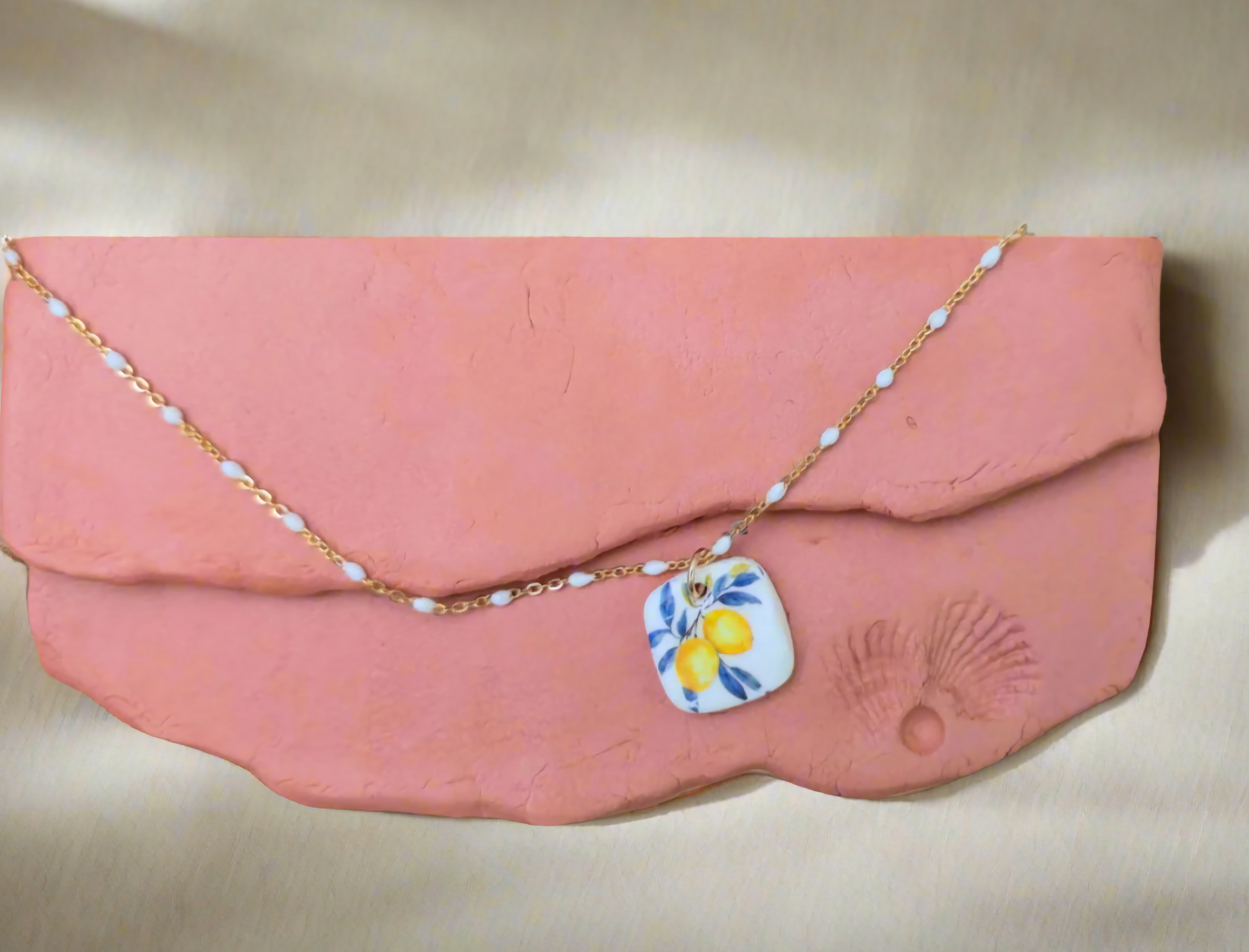 Pink clutch with a necklace draped over it on a beige background