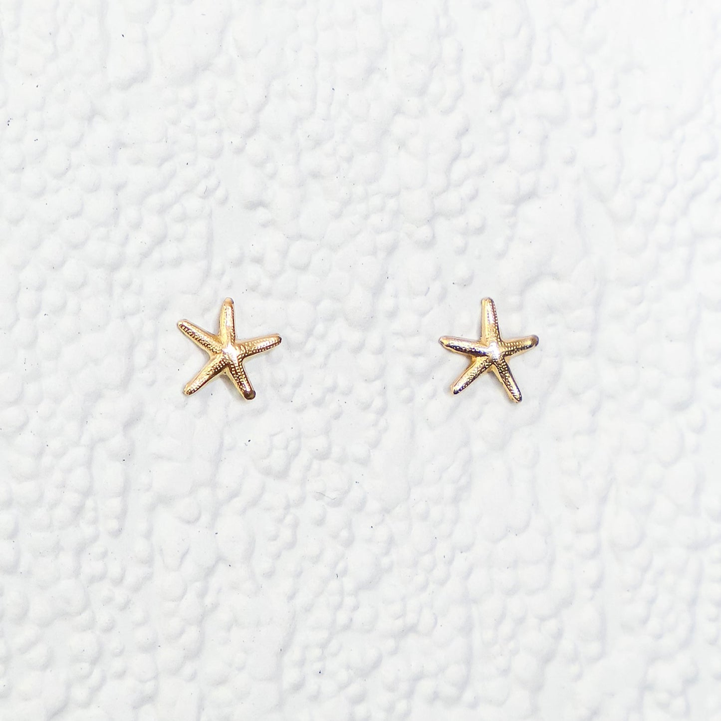 Gold star-shaped earrings on a textured white background