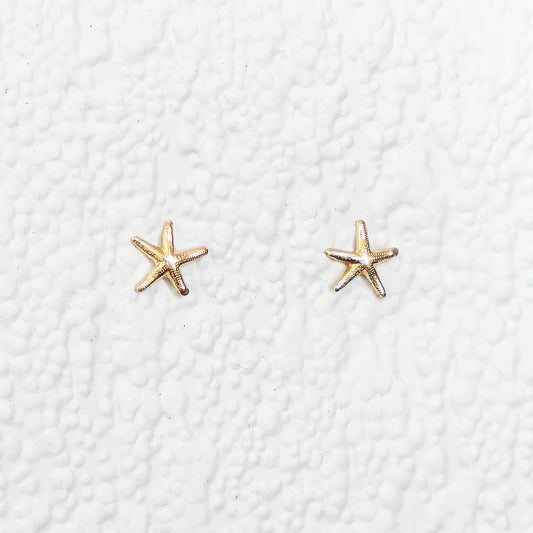 Gold star-shaped earrings on a textured white background